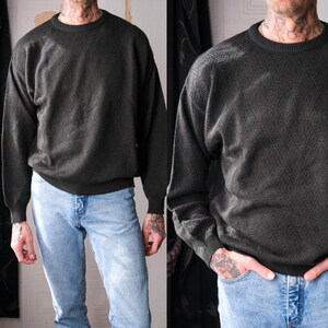 May include: Dark green sweater with a textured pattern. The sweater has a crew neck and long sleeves. The model is wearing light blue jeans.
