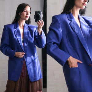 May include: A vibrant blue blazer with a classic design. The blazer features a tailored fit, a notched lapel, and two front pockets. The long sleeves have buttoned cuffs. The blazer is made of a textured fabric and is shown in a medium shot.