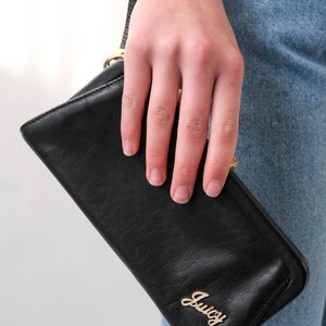 May include: A black leather wallet with a gold Juicy Couture logo. The wallet is being held by a hand.