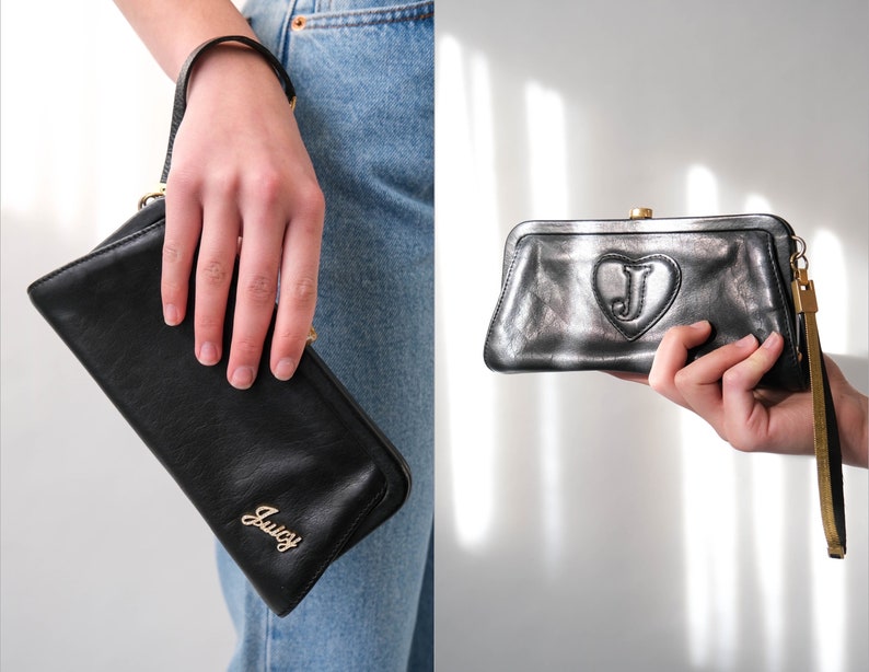 May include: Black leather clutch with a gold Juicy Couture logo and a gold heart with a J inside. The clutch has a wrist strap.