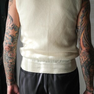 Peut inclure: Un pull sans manches cr&egrave;me avec un ourlet c&ocirc;tel&eacute; et une texture douce. Le pull est associ&eacute; &agrave; un pantalon noir brillant. L'ensemble est simple et classique, adapt&eacute; pour &ecirc;tre port&eacute; seul ou superpos&eacute;.