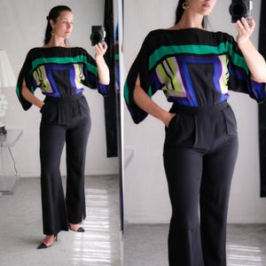 Könnte beinhalten: Schwarzer Jumpsuit mit einem Oberteil mit einem farbenfrohen geometrischen Design in Grün, Blau und Lila. Der Jumpsuit hat eine Hose mit weitem Bein und einen Bootsausschnitt. Die Ärmel sind an den Seiten offen.