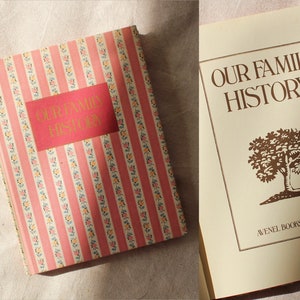 Op de afbeelding: Een vintage boek getiteld "Our Family History" met een roze en witte gestreepte omslag en een bruine boomillustratie op de achterkant. Het boek is uitgegeven door Avenel Books, New York.