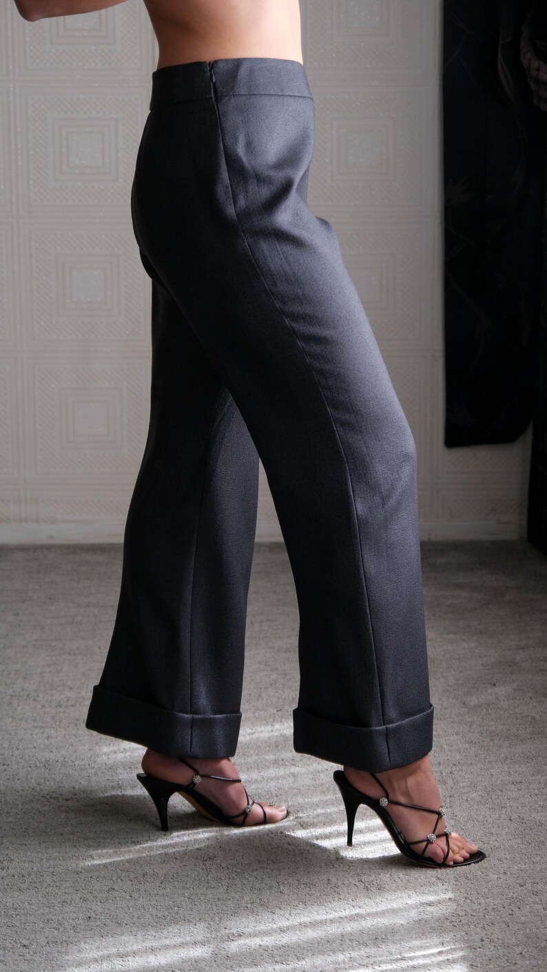 May include: Dark gray wide-leg trousers with a cuffed hem. The pants are paired with black high-heeled sandals with delicate straps and rhinestone accents. The fabric appears to be a smooth, woven material.