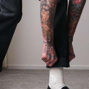 Peut inclure: Mocassins en cuir noir avec boucle dor&eacute;e. Les chaussures sont port&eacute;es avec des chaussettes blanches et un jean denim fonc&eacute;. L'image met l'accent sur les chaussures et le bas des jambes.