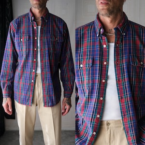 May include: A long-sleeved plaid shirt in blue, red, and green. The shirt features two chest pockets and a button-down collar. The shirt is worn with beige trousers.