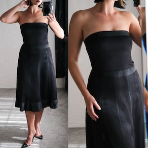 May include: A black strapless dress with a fitted bodice and a flowing skirt. The skirt has a subtle textured pattern and a ruffled hem.