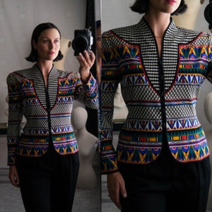 May include: A black and white patterned blazer with colorful geometric designs. The blazer has a V-neck and a button closure.