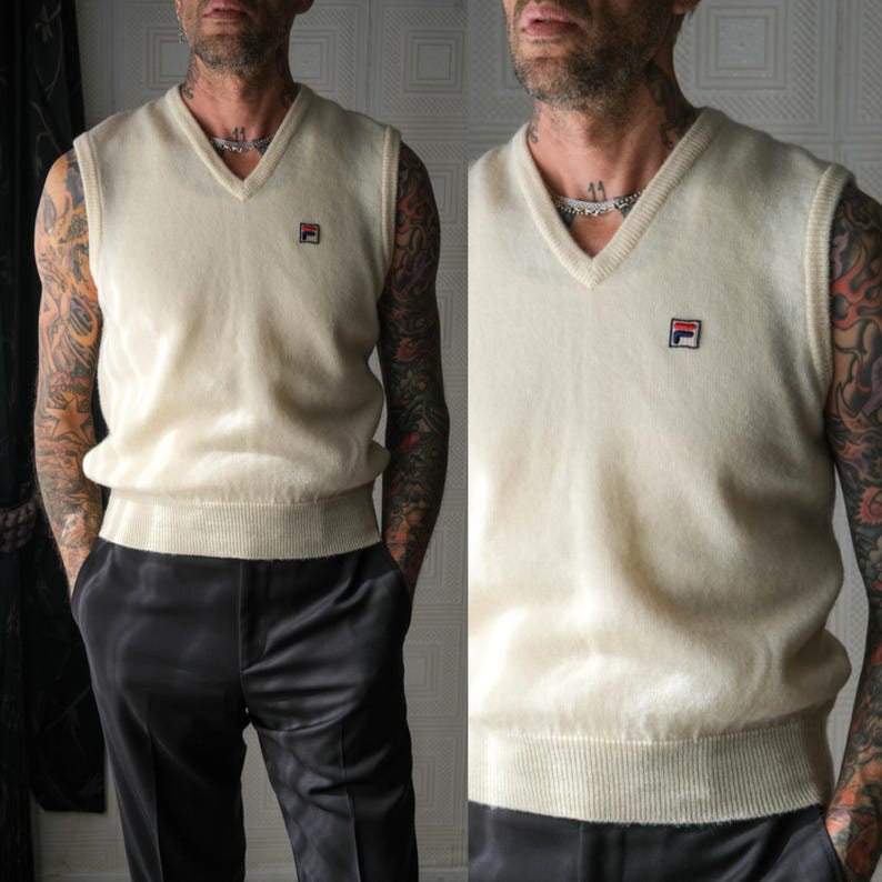 Peut inclure: Gilet de pull cr&egrave;me &agrave; col en V avec un petit logo sur la poitrine. Le gilet a un ourlet c&ocirc;tel&eacute; et une coupe classique. Le logo est un carr&eacute; avec un design rouge et bleu. Le gilet est associ&eacute; &agrave; un pantalon noir.