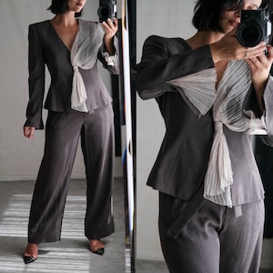 Può includere: Un tailleur pantalone marrone e bianco con motivo e un dettaglio di fiocco di velo bianco sul collo. La giacca ha un colletto a revers e maniche lunghe. I pantaloni sono a gamba larga e hanno una gamba dritta.