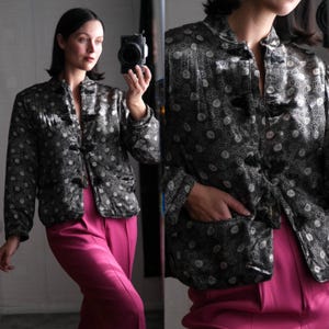 Può includere: Una giacca di raso con motivo bianco e nero con colletto alla coreana e chiusura con bottoni. La giacca ha una tasca sul lato sinistro ed è indossata con un paio di pantaloni rosa.