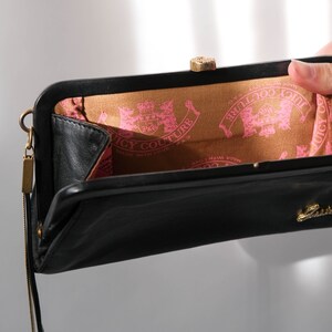 May include: Black leather clutch purse with a gold clasp and a gold chain strap. The inside lining is brown with a pink "Juicy Couture" logo.