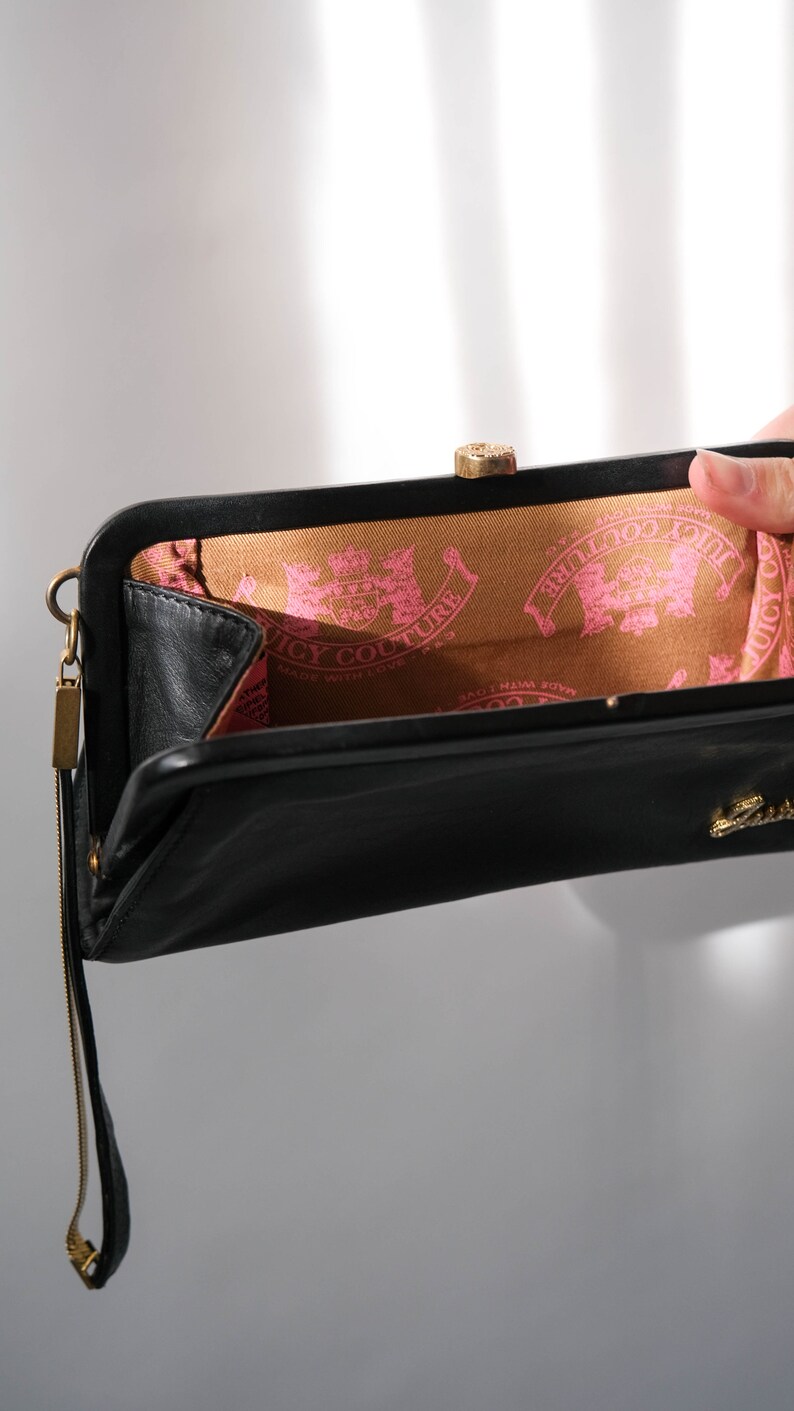 May include: Black leather clutch purse with a gold clasp and a gold chain strap. The inside lining is brown with a pink "Juicy Couture" logo.