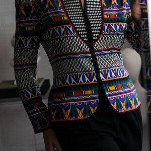 May include: A black and white patterned blazer with a colorful geometric design. The blazer has a V-neck and a button closure. The model is wearing black pants.