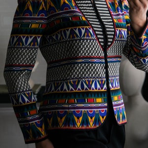 May include: A black blazer with a colorful geometric pattern. The pattern features a variety of colors, including red, yellow, blue, green, and white. The blazer has a V-neck and a black collar.