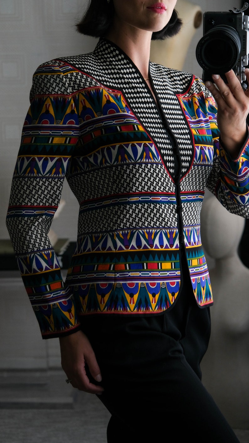 May include: A black blazer with a colorful geometric pattern. The pattern features a variety of colors, including red, yellow, blue, green, and white. The blazer has a V-neck and a black collar.