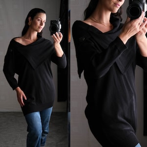 May include: A black cowl neck sweater with a draped neckline. The sweater is made of a soft, comfortable fabric and has a relaxed fit.