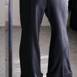 May include: Dark gray flared trousers with a tailored fit. The pants feature a high waist, vertical seams, and cuffed hems. The model is wearing black heeled sandals. The fabric appears to be a smooth, woven material.