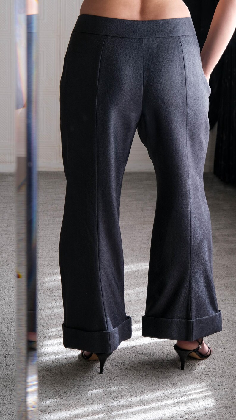 May include: Dark gray flared trousers with a tailored fit. The pants feature a high waist, vertical seams, and cuffed hems. The model is wearing black heeled sandals. The fabric appears to be a smooth, woven material.