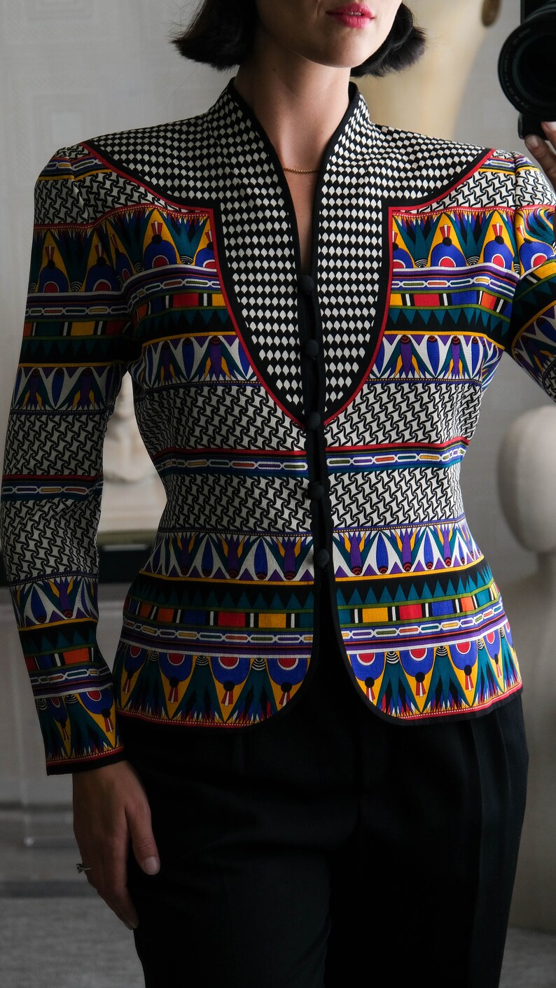 May include: A black and white patterned blazer with a colorful geometric design. The blazer has a mandarin collar and a button closure.