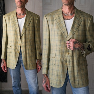 May include: A light tan blazer with a blue plaid pattern. The blazer has two front pockets and a single-button closure. The jacket is worn over a white undershirt and blue jeans. The blazer has a classic, tailored fit.
