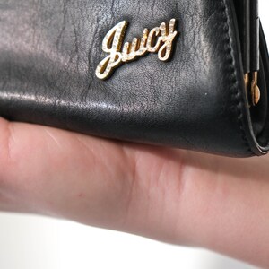 May include: Black leather clutch purse with a gold metal Juicy Couture logo.