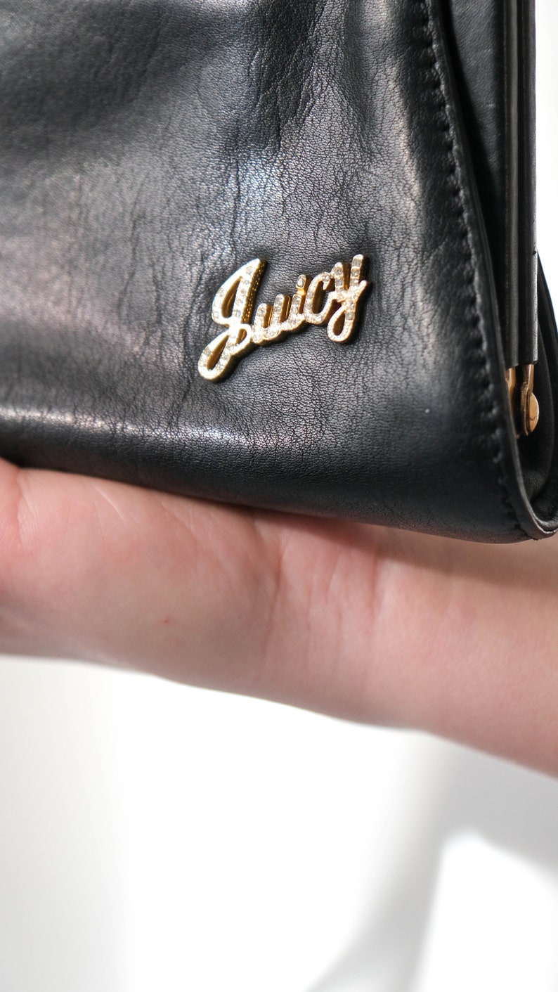 May include: Black leather clutch purse with a gold metal Juicy Couture logo.