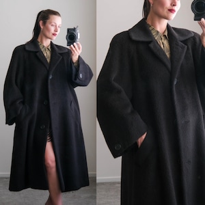 May include: A long, black coat with a classic design. The coat features a collared neckline, button closures, and pockets. The coat is made of a textured fabric and has a knee-length hemline. The coat is a versatile piece for any wardrobe.