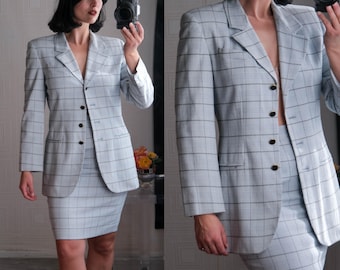 Puede incluir: Un traje de falda azul claro a cuadros, con una chaqueta y una falda. La chaqueta tiene un cuello de muesca, un cierre de botón simple y dos bolsillos de solapa. La falda es de largo hasta la rodilla y tiene una silueta recta.