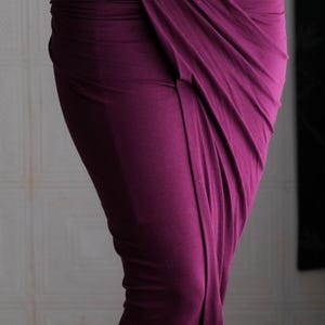 May include: A draped, midi-length skirt in a deep plum color. The fabric is gathered and wrapped, creating a unique asymmetrical design. The skirt appears to be made of a soft, flowing material.