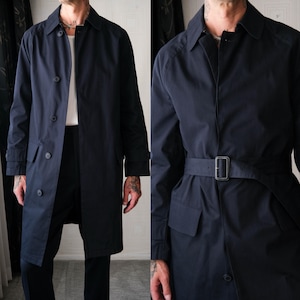 May include: A navy blue trench coat with a button-up front, a belt, and pockets. The coat has a classic design and is made of a smooth, durable fabric. The coat is a versatile outerwear piece.
