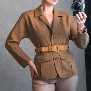 May include: A brown blazer with a matching belt and tan pants. The blazer has two front pockets and a button closure. The belt is light brown and cinches the waist. The pants are a neutral color.