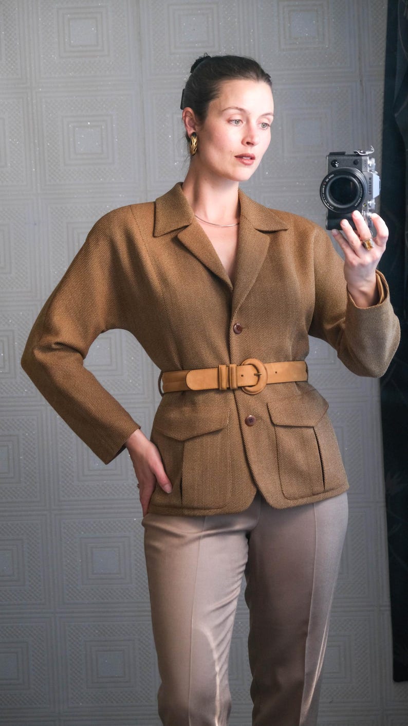 May include: A brown blazer with a matching belt and tan pants. The blazer has two front pockets and a button closure. The belt is light brown and cinches the waist. The pants are a neutral color.