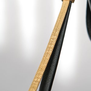 May include: A black leather strap with a gold chain detail. The strap is attached to a gold ring.