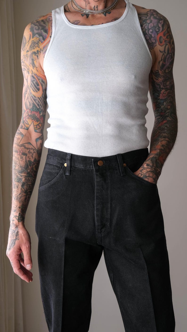 Peut inclure: D&eacute;bardeur blanc c&ocirc;tel&eacute; et jean en denim noir. Le jean a une conception classique &agrave; cinq poches avec une fermeture boutonn&eacute;e et zipp&eacute;e. Le mod&egrave;le a des tatouages sur les deux bras.