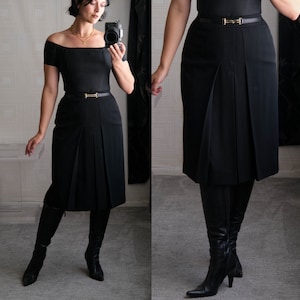 May include: A black skirt with a high waist and pleats. The skirt has a gold buckle belt and is paired with black knee-high boots.