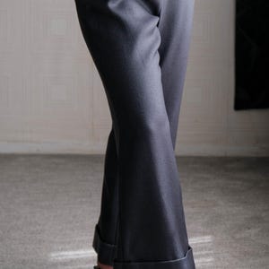 May include: Charcoal gray trousers with a slight flare at the hem. The pants have a tailored fit and are cuffed at the ankles. The model is wearing black strappy heels with decorative embellishments.