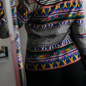 May include: A black and white patterned blouse with a colorful geometric design. The blouse has a high collar and long sleeves.