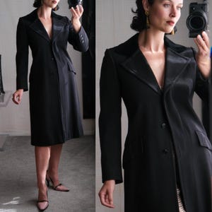 May include: A black long-sleeved coat with a satin collar and a single button closure. The coat has a fitted silhouette and a slightly flared hem.