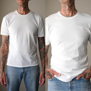 May include: A plain white short-sleeved t-shirt with a crew neckline. The garment is constructed from a solid white fabric and features a standard fit with short sleeves and a rounded collar, providing a clean and simple appearance for everyday wear.