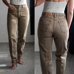 May include: A pair of brown denim jeans with a classic five-pocket design. The jeans have a straight leg fit and a high waist. The back features two pockets and a leather patch. The jeans are a neutral color, suitable for various outfits.