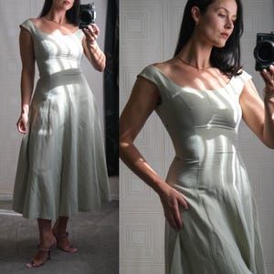 Peut inclure: Une robe vert clair avec un col en cœur et des manches courtes. La robe a un corsage ajusté et une jupe évasée qui arrive à mi-mollet. La robe est faite d'un tissu léger et semble être de style vintage.