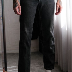 May include: A person wearing black denim jeans with a white t-shirt and black leather loafers with gold buckles.
