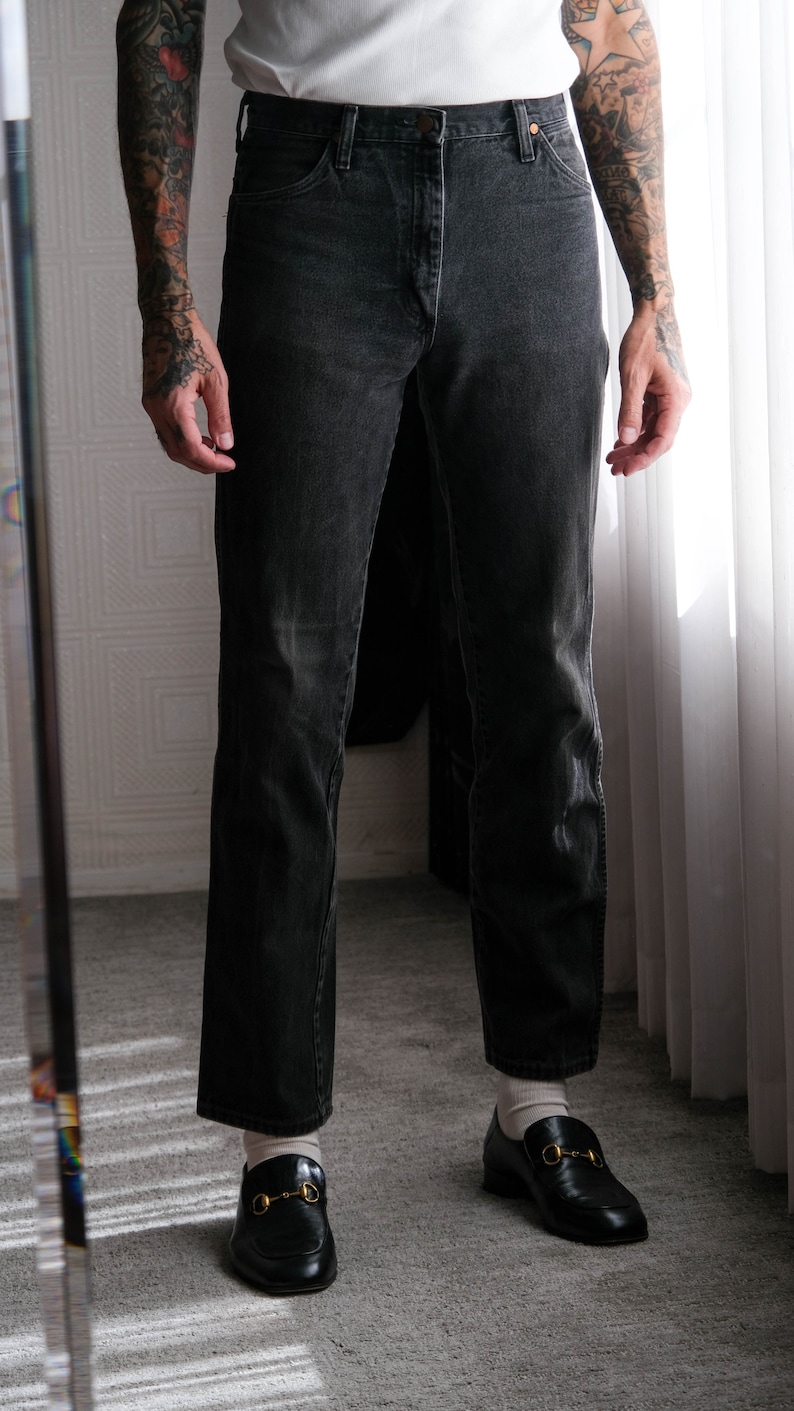 May include: A person wearing black denim jeans with a white t-shirt and black leather loafers with gold buckles.