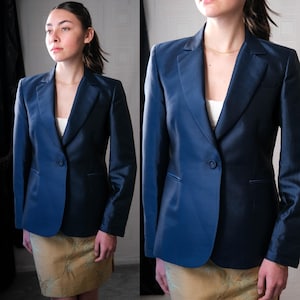May include: A navy blue blazer with a single-button closure. The blazer has a satin finish and a notched lapel. The model is wearing a white top and a gold-colored skirt.