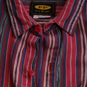 May include: A button-down shirt with vertical stripes in red, blue, green, and white. The shirt has a collar and red buttons. The label reads "FP Free People."