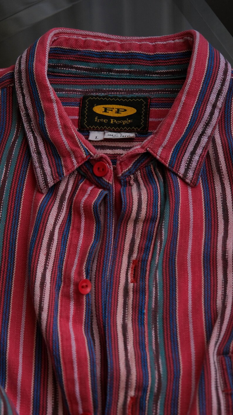 May include: A button-down shirt with vertical stripes in red, blue, green, and white. The shirt has a collar and red buttons. The label reads "FP Free People."