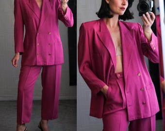 Op de afbeelding: Een magenta dubbelrijig blazer en bijpassende broekpak. De blazer heeft een reverskraag en twee zakken. De broek heeft een rechte pijp.