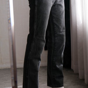 May include: A person wearing black jeans and black loafers with gold accents. The person is standing on a carpeted floor.
