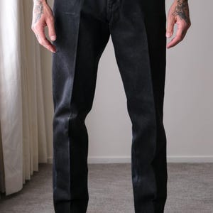 Peut inclure: Pantalon en denim noir de coupe classique. Le pantalon a une fermeture boutonn&eacute;e et une jambe droite. Le mod&egrave;le porte des mocassins en cuir noir avec des accessoires dor&eacute;s. Le pantalon est d&eacute;lav&eacute; fonc&eacute;.